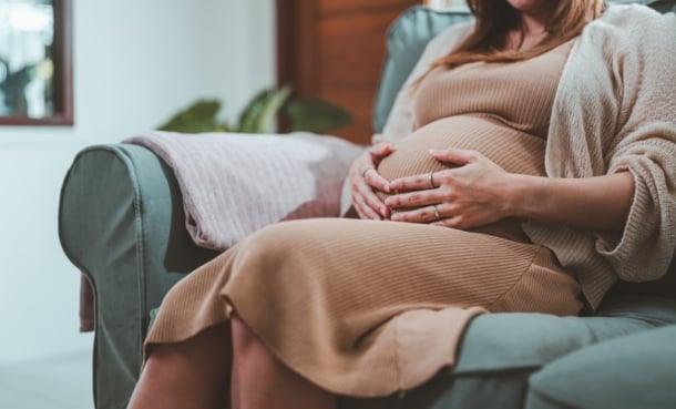 Pregnant woman sits on sofa with hands on stomach