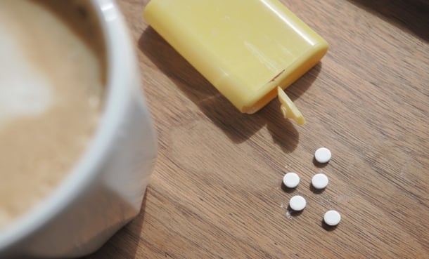 artificial sweeteners laid out on a wooden table next to cup of coffee