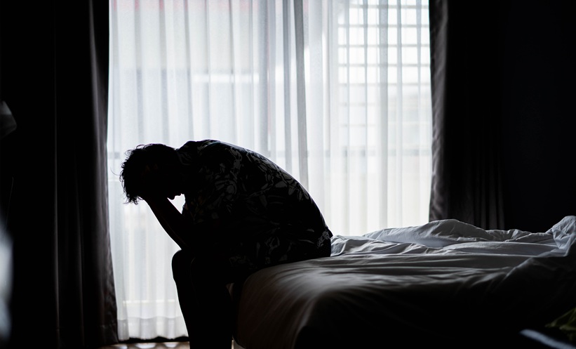 Person who is suffering evere mental health sisues and sitting on the bed with his head in his hands