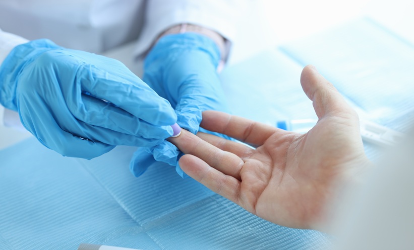 Health professional wearing blue latex surgical gloves takes finger prick test from person's hand