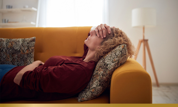 Woman-with-headache-and-stomach-pain-lying-on-a-couch-at-home