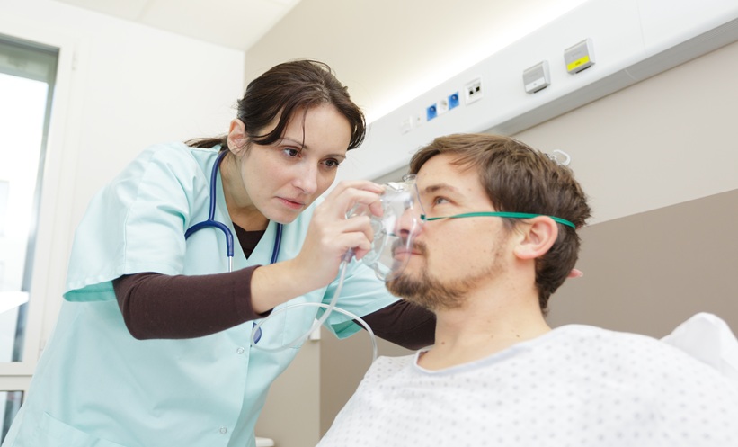 Healthcare professional adjusting an oxygen mask on a patient, illustrating respiratory complications associated with cystic fibrosis lung disease.