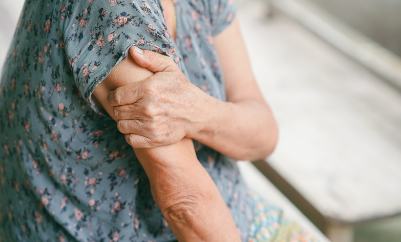 Senior woman suffering from arm pain, holding her shoulder due to muscle ache or arthritis.