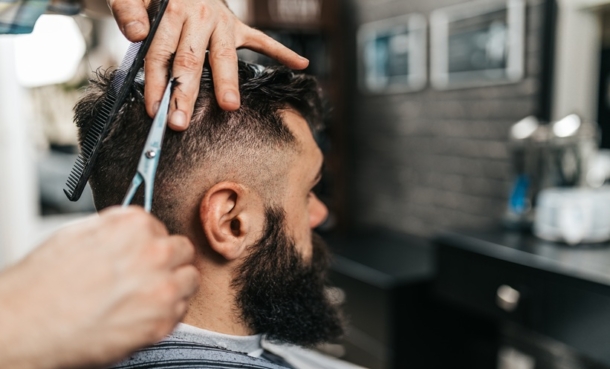 Barber cutting a male customer’s short hair, highlighting scalp sun exposure and skin cancer prevention.
