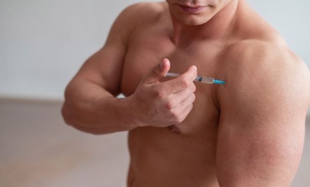 Unrecognizable shirtless bodybuilder man puts himself an injection of growth hormone.