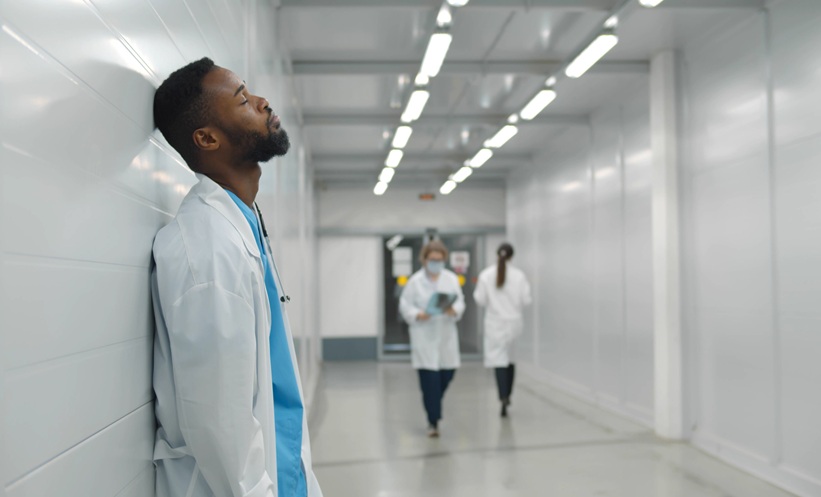 Healthcare professional standing at a hospital workstation, illustrating healthcare worker burnout and workplace stress.