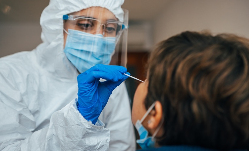 Close up of female health Professional in PPE introducing a nasal swab to a senior female patient at her house.