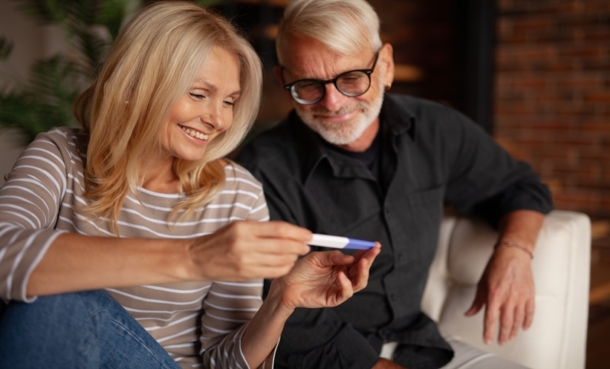 Happy mature parents with a pregnancy test in their hands are sitting at home.