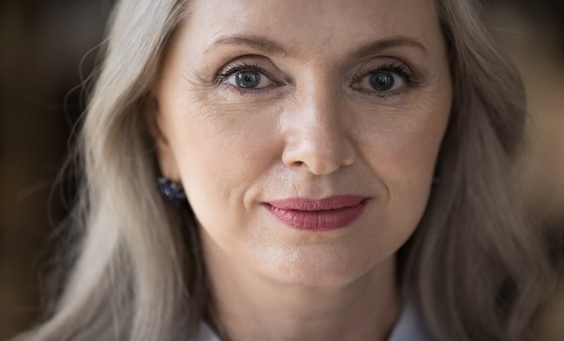 Close-up portrait of a mature woman showing natural facial aging signs, including fine lines around the eyes and facial skin texture.