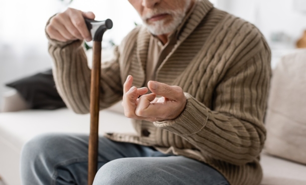 senior man with parkinson disease holding walking cane while sitting on couch at HOME