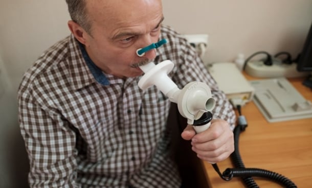 Man sitting down wearing nose clip blows into spirometer