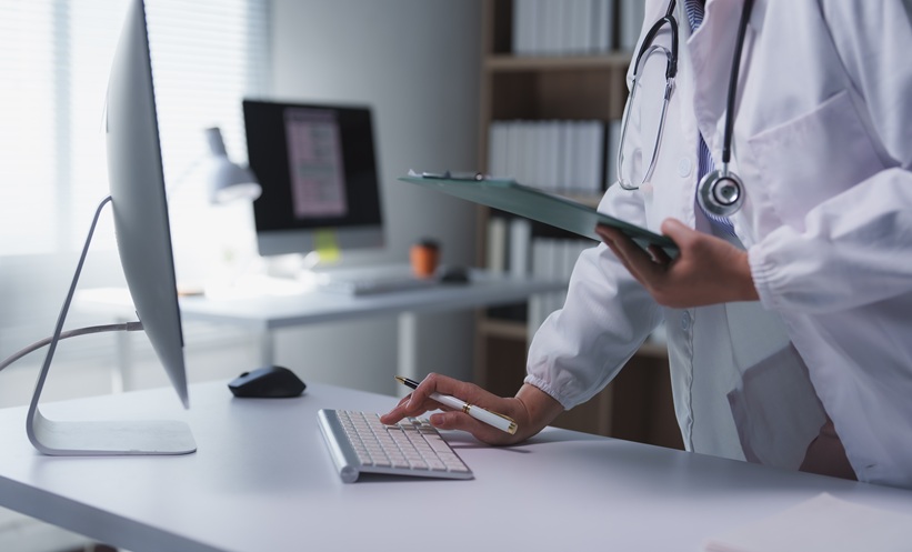 Doctor standing with clipboard and pen looks at results on computer