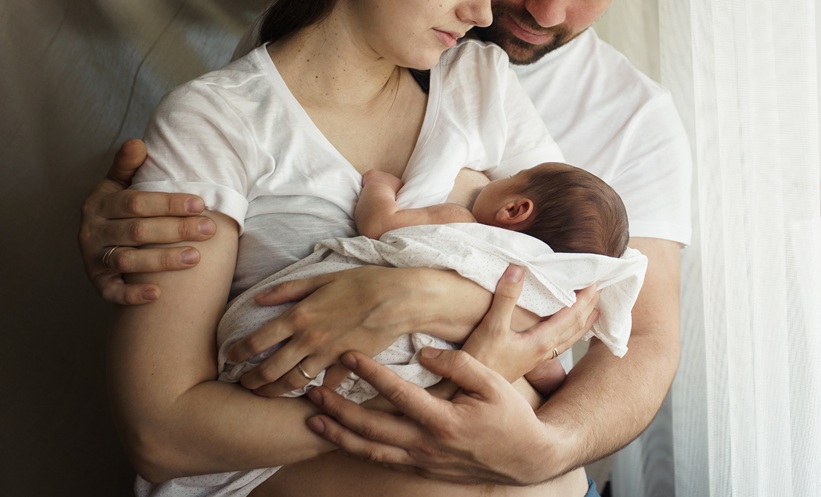 Parents holding newborn baby who is breastfeeding