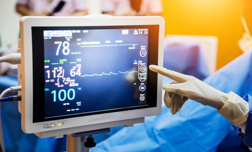 Doctor with gloved hand points at telemetry screen with readings of a persons heart rate